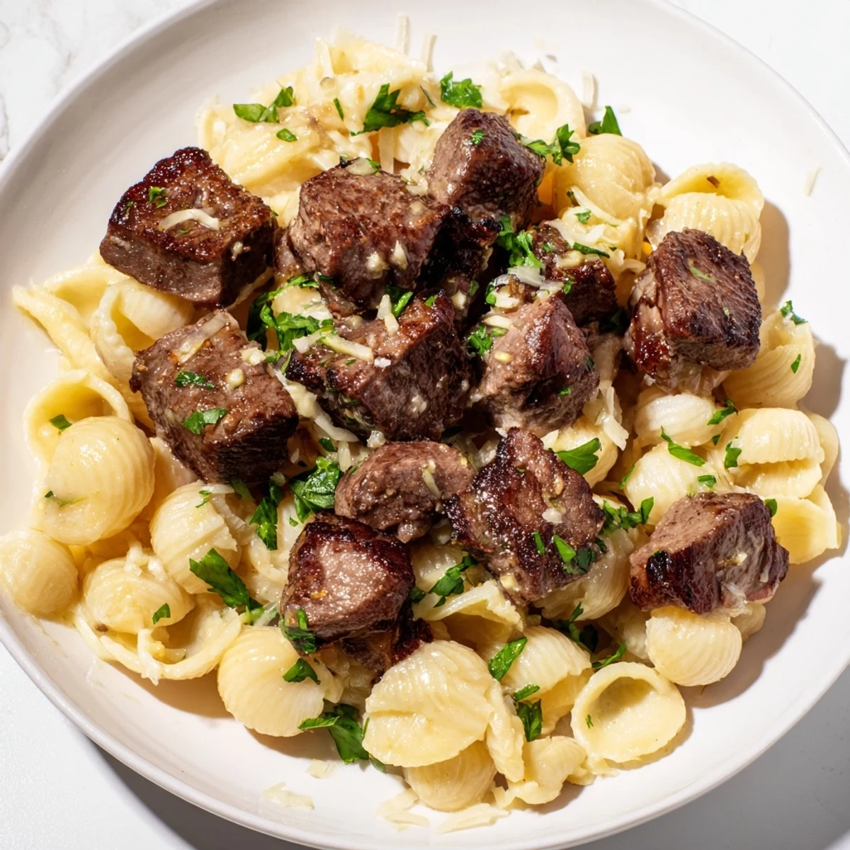 A close-up of tender garlic butter steak bites spooned over cheesy shells, ready to eat.