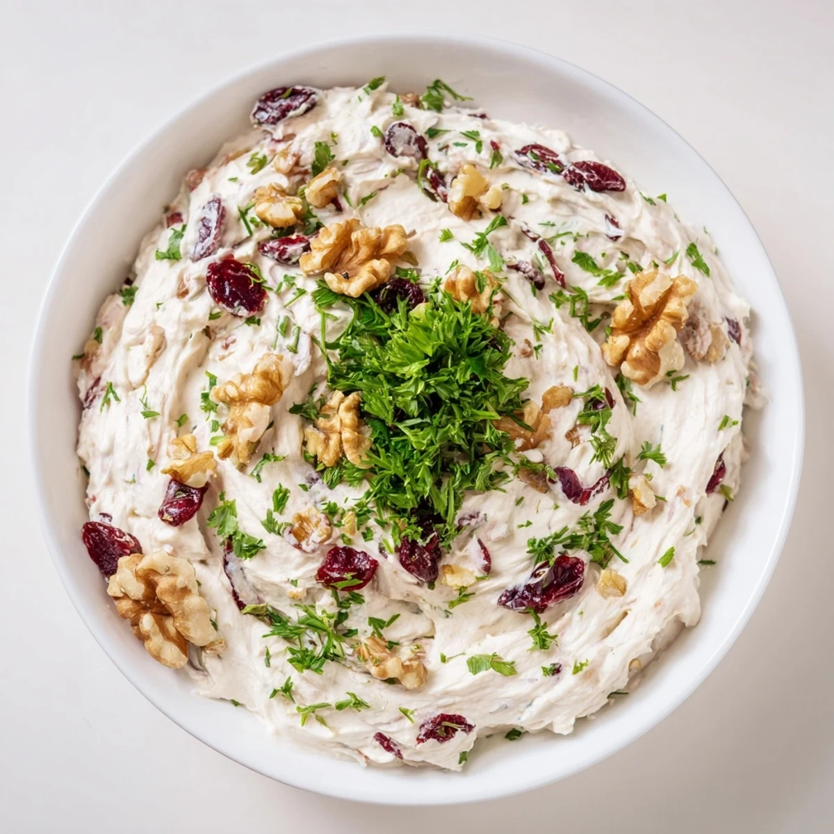 A bowl of delicious Lightened Holiday Cream Cheese Dip, with visible herbs alongside the cream cheese and cranberries.