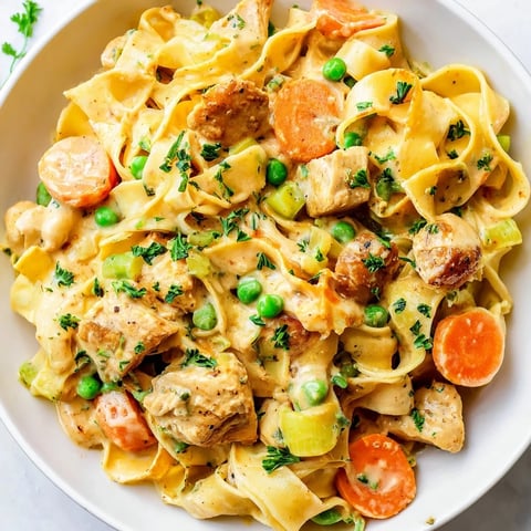 Steaming bowl of creamy chicken and egg noodles, with visible vegetables and a light parsley garnish.