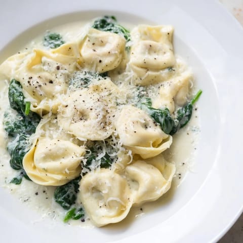 A close-up of Creamy Spinach Alfredo Tortellini, ready to eat, with a rich, white sauce and greens.