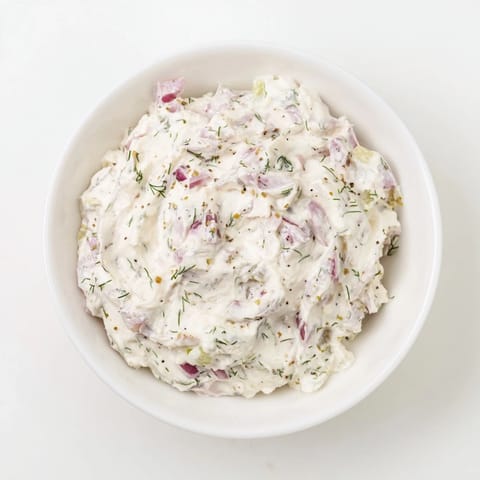A close-up view of the sweet and sour pickle relish dip with flecks of fresh dill and red onion.