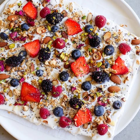 Homemade frozen fruit yogurt bark with granola, nuts, and a delightful berry topping.