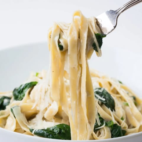 A close-up of Creamy Garlic Spinach Pasta showing steaming fettuccine tossed with fresh spinach and creamy garlic sauce.