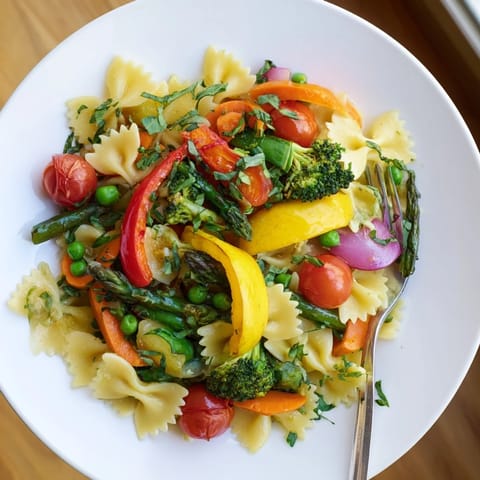 A close-up of Rainbow Veggie Pasta Primavera highlights fresh herbs and a light garlic olive oil sauce perfect for weeknight dinners.  