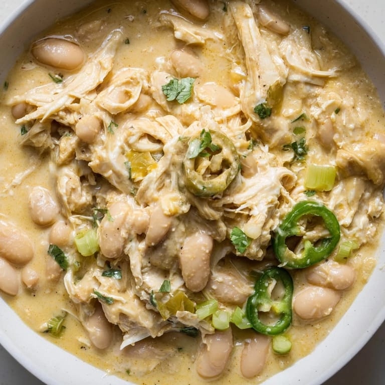 Close-up of a steaming bowl of creamy white chicken chili with beans, full of tender chicken and veggies.