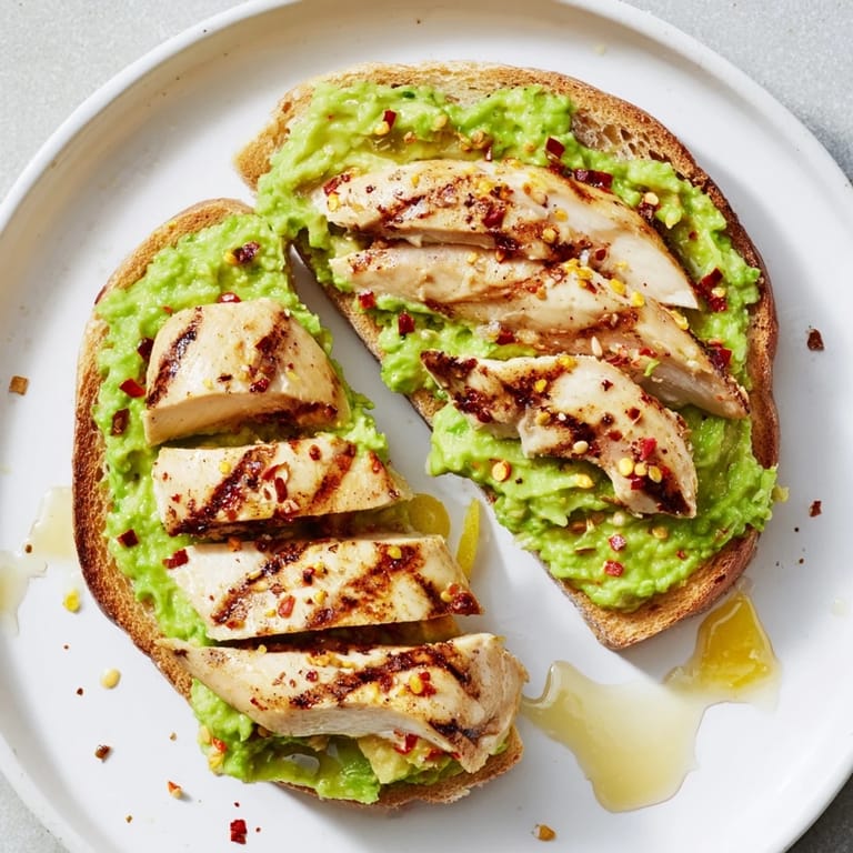 This hearty Smashed Avocado Chicken Toast is plated with chili flakes and honey for a savory-sweet finish.