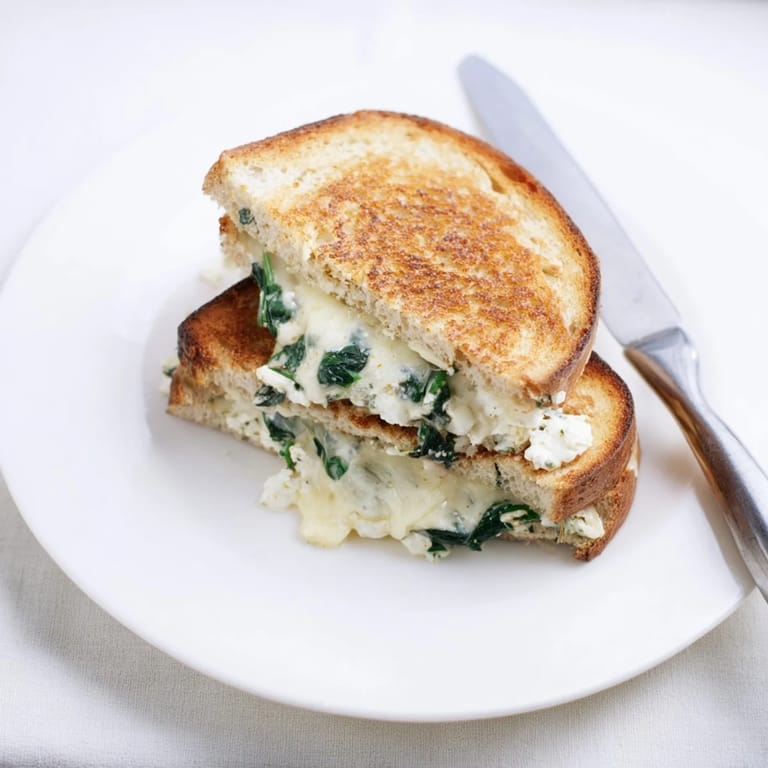 A close-up of Feta & Spinach Stuffed Grilled Cheese reveals a vibrant green spinach and tangy feta filling between thick sourdough slices.
